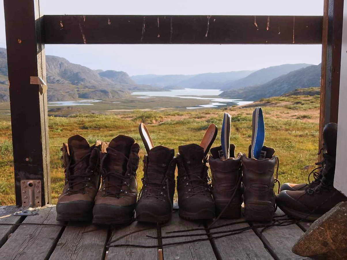 Several pairs of hiking boots lined up and drying in the sun in front of one of the huts on the Arctic Circle Trail