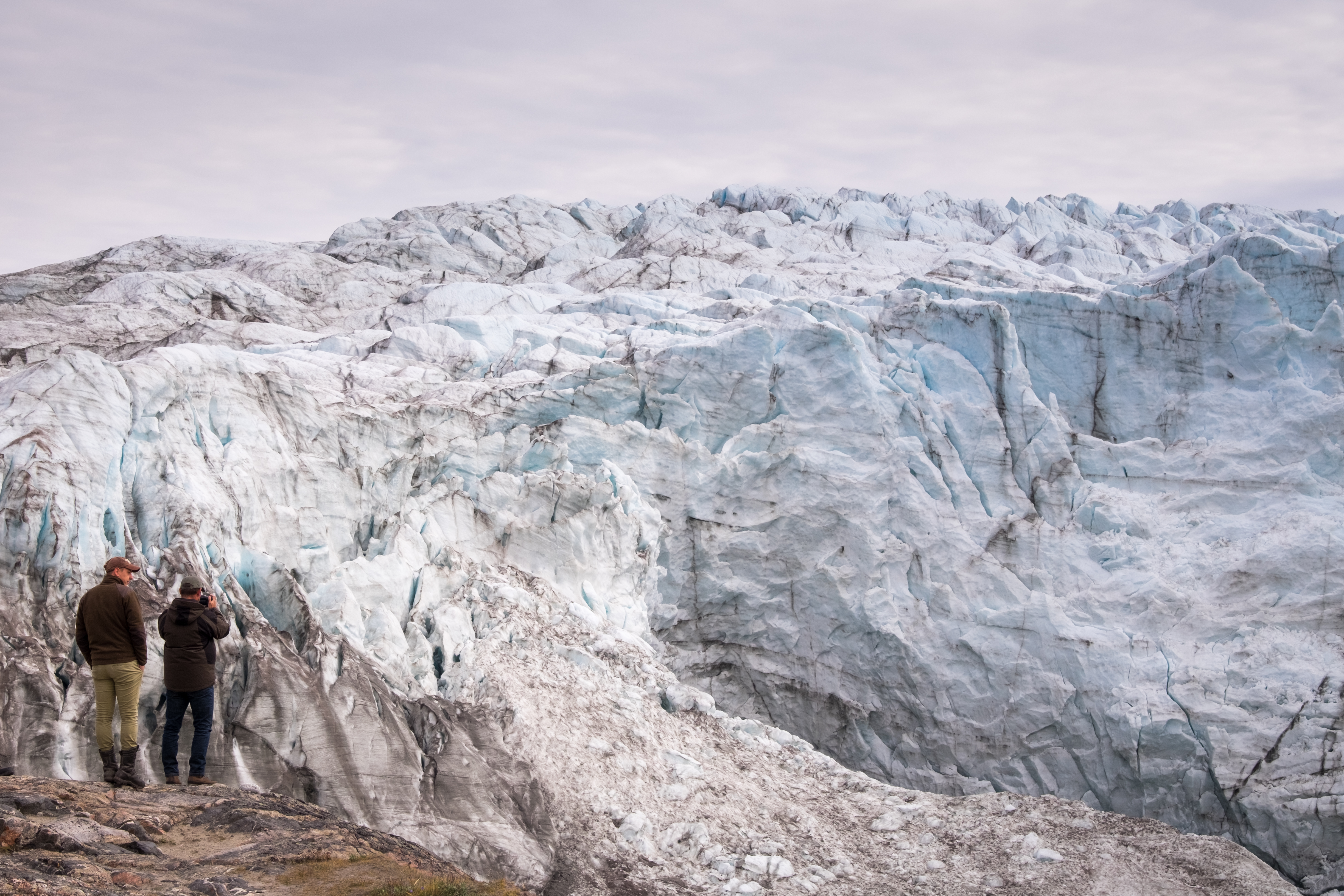 Two visitors standing in front of the massive ice face of the Russell Glacier near Kangerlussuaq